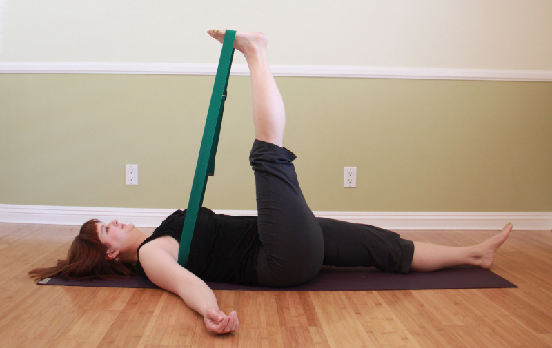 Addie deHilster practicing a reclining leg stretch as a Yin Yoga pose with props 