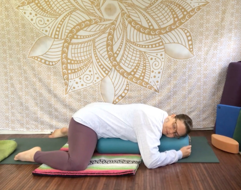 Addie deHilster demonstrating Frog Pose on a bolster for Yin Yoga Teacher Training online.