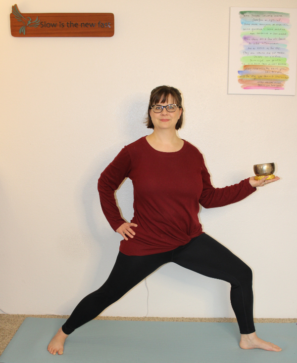 Addie deHilster in Warrior Pose holding a bell, demonstrating the movement-based mindfulness course.