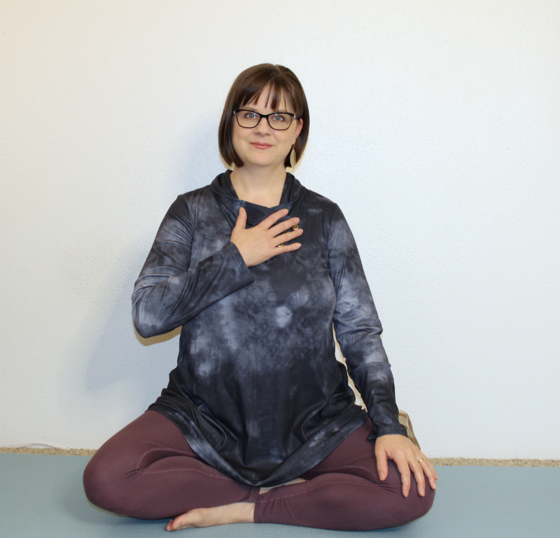 Picture of Mindful Movement Teacher, Addie deHilster, seated on a cushion and smiling with her hand on her heart.