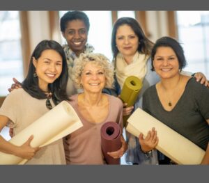 Group of people smiling and holding mats, demonstrating the bio psycho social spiritual benefits of mindful movement.