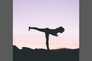 Silhouette of a movement teacher demonstrating a yoga pose outdoors at sunset.