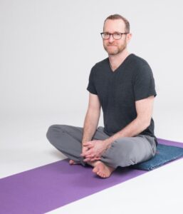 Picture of Jivana Heyman sitting on a yoga mat, demonstrating accessible meditation.