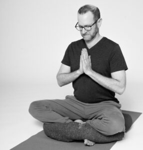 Jivana Heyman using a blanket to demonstrate an accessible meditation posture.