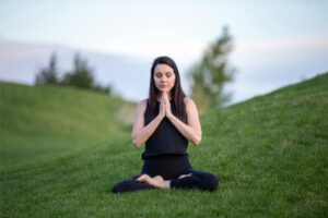 Woman meditating in a green field, practicing trauma-informed yoga.